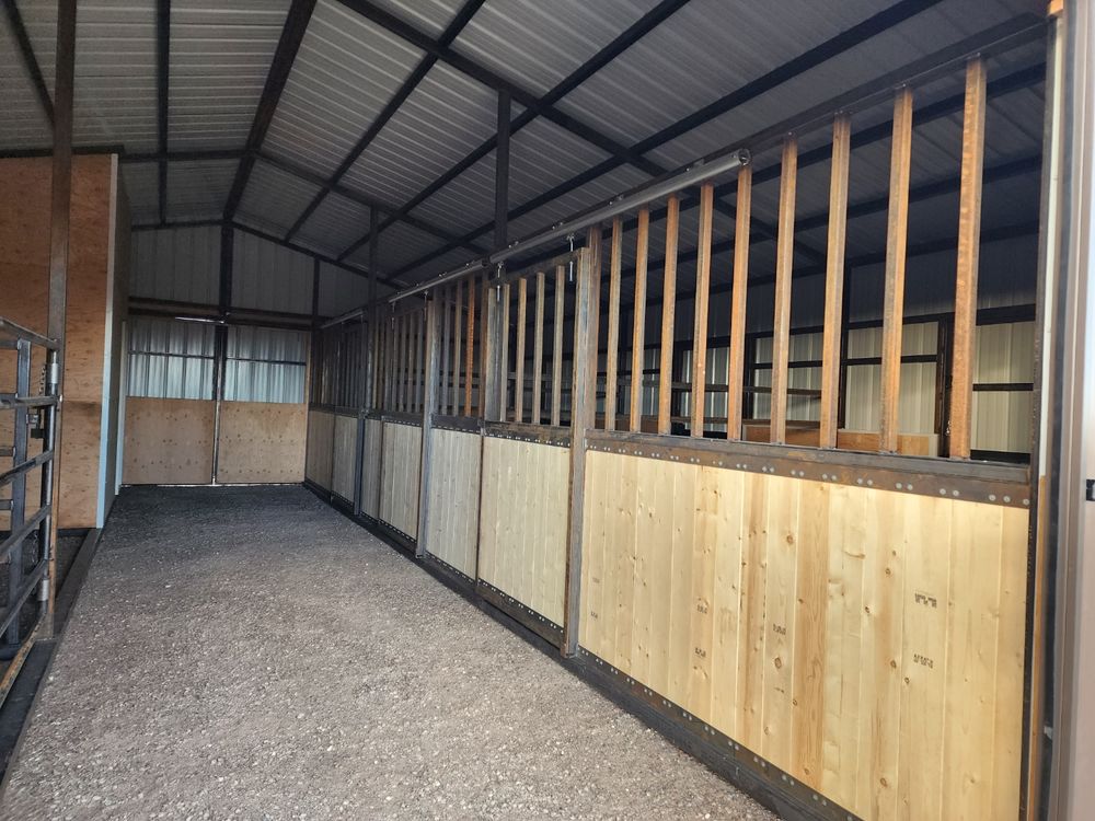 Interior center breezeway of a metal horse barn with a row of sliding stall fronts down one side