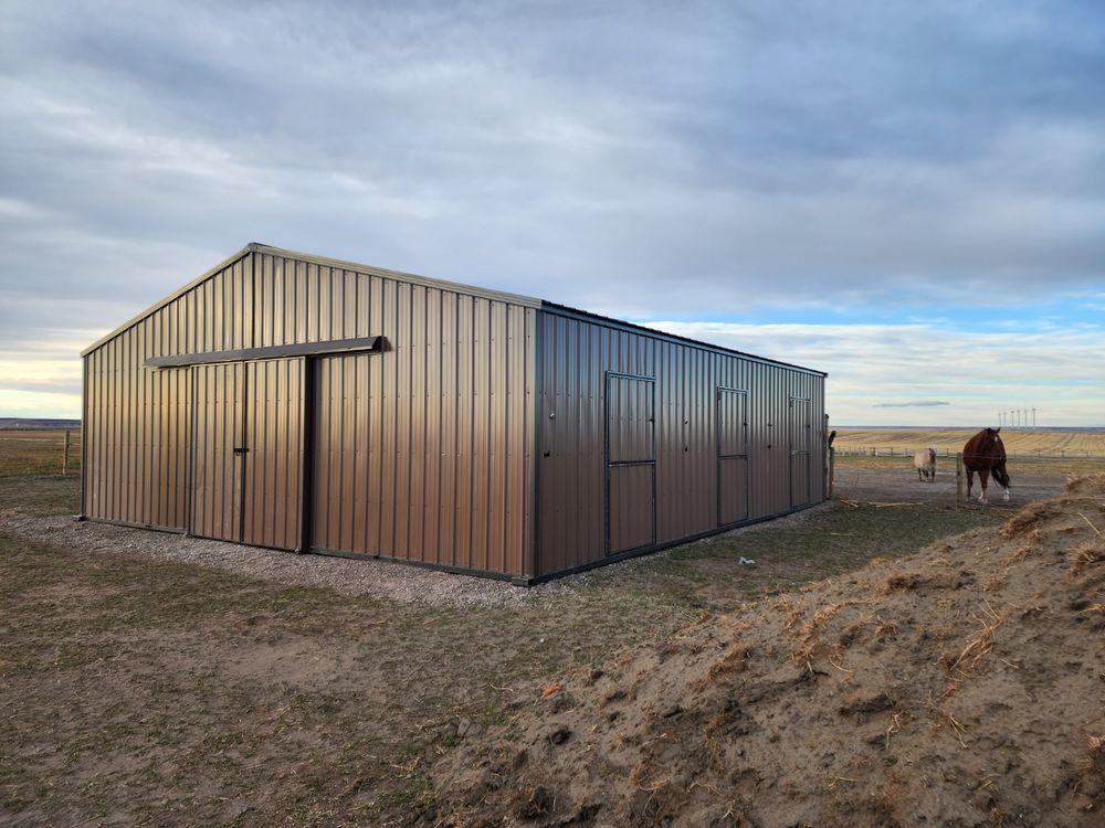 34 by 36 foot metal horse barn on a compacted gravel pad in Montana with horses grazing nearby