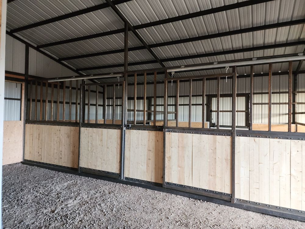 Row of 11 foot by 11 foot horse stalls with sliding fronts inside a welded steel metal barn