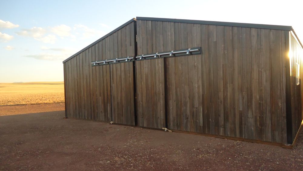 Gable end of a 34 foot wide by 36 foot long metal horse barn clad in 26 gauge antique barnwood plank woodgrain steel siding with twin sliding barn doors