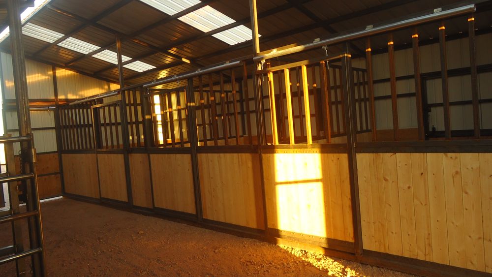Interior stall run inside a woodgrain metal horse barn with steel framed sliding stall fronts and wood plank lower panels