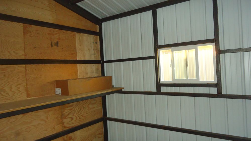 Corner tack room inside a metal horse barn with plywood walls, a shelf and a sliding window